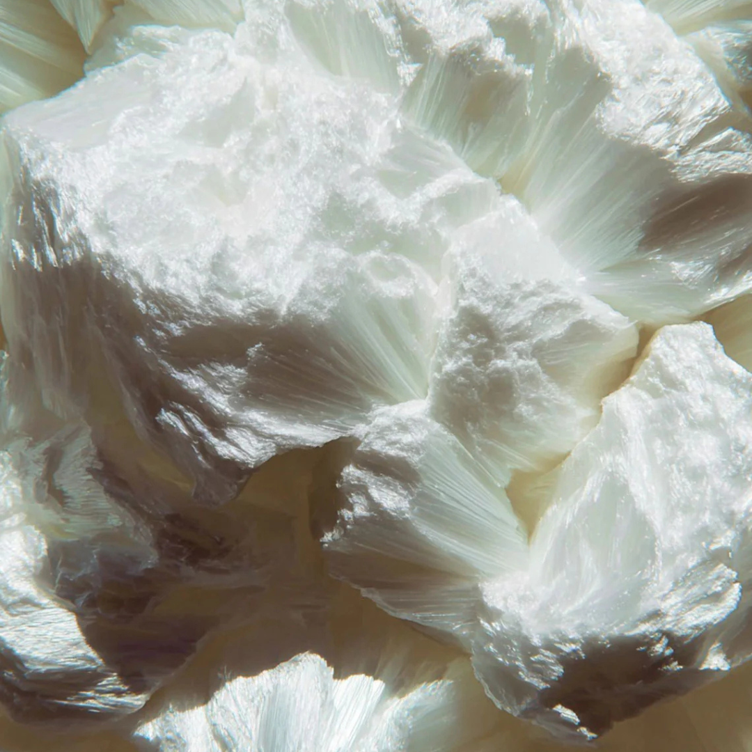 A close-up, abstract view of a white, fibrous, crystalline mineral with a silky sheen.
