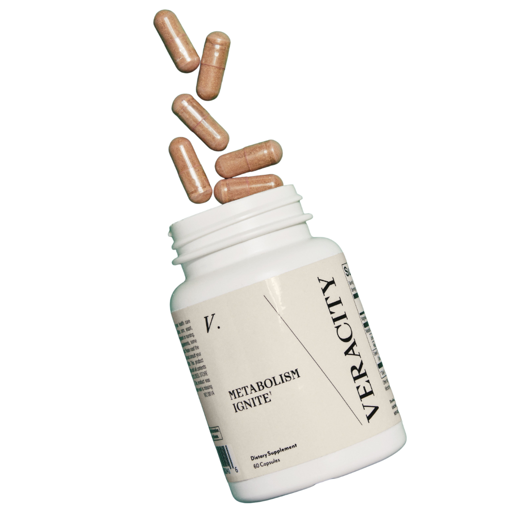 Veracity Metabolism Ignite supplement capsules spilling out of an open white bottle against a black background.