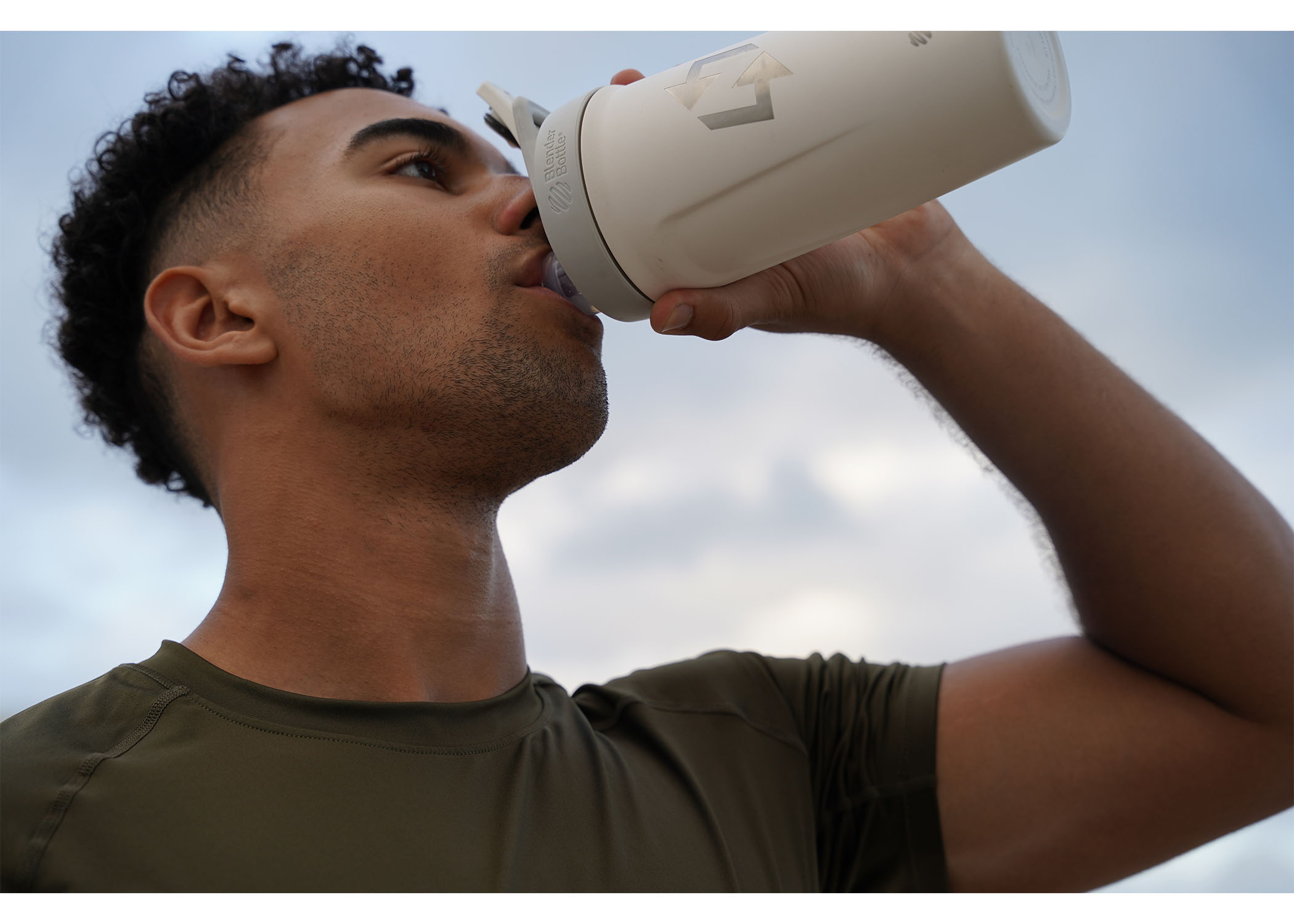 Person drinking from a white bottle outdoors.