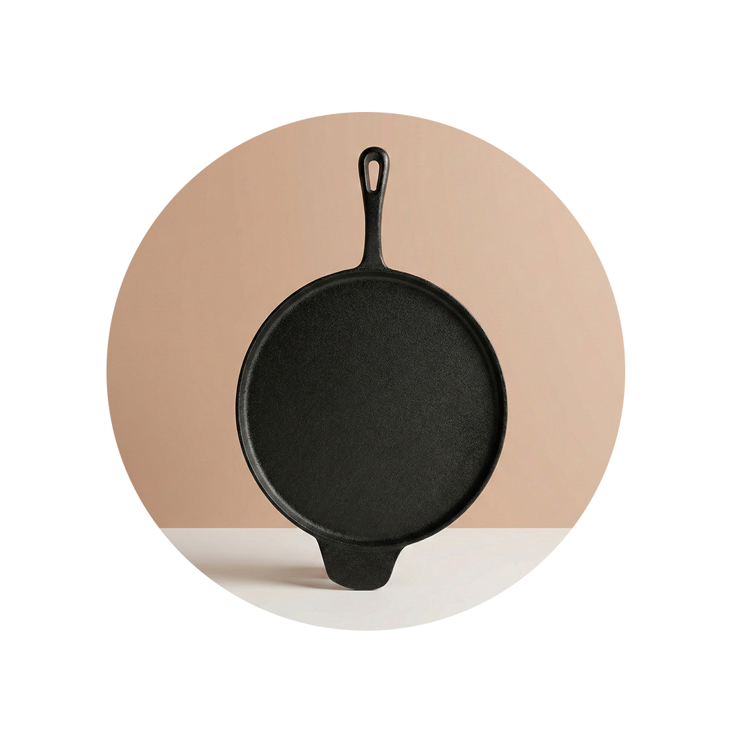 A round, black cast iron griddle with a handle, standing upright on a white surface.