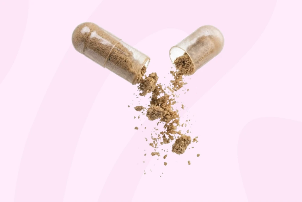 A transparent capsule is opened, with brown powder spilling out against a light pink background.