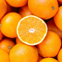A close-up of many whole oranges with one orange cut in half.