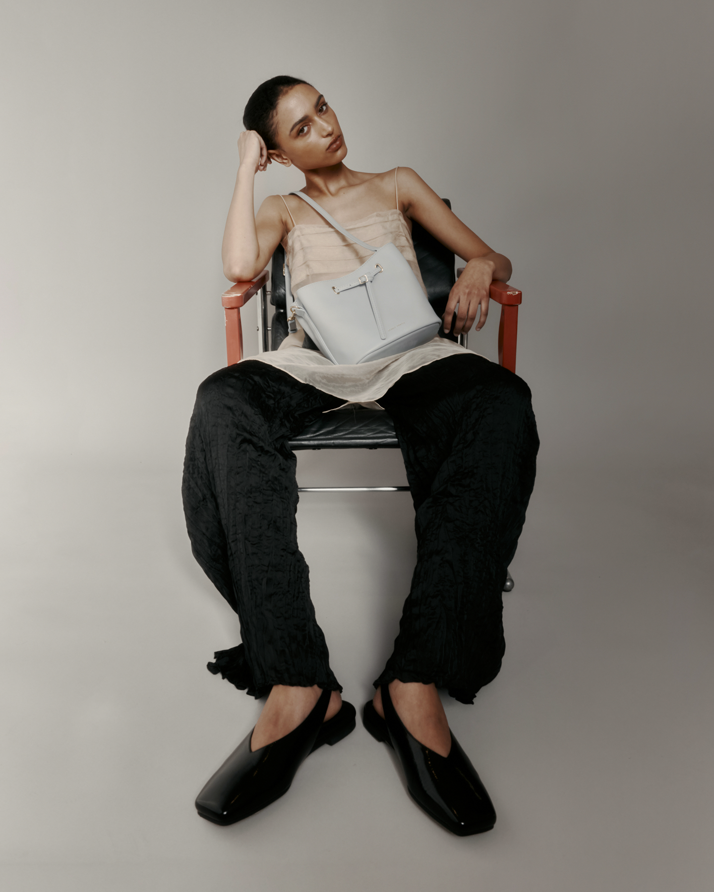 Person sitting on a chair wearing a sleeveless top, dark pants, and holding a light-colored bag.