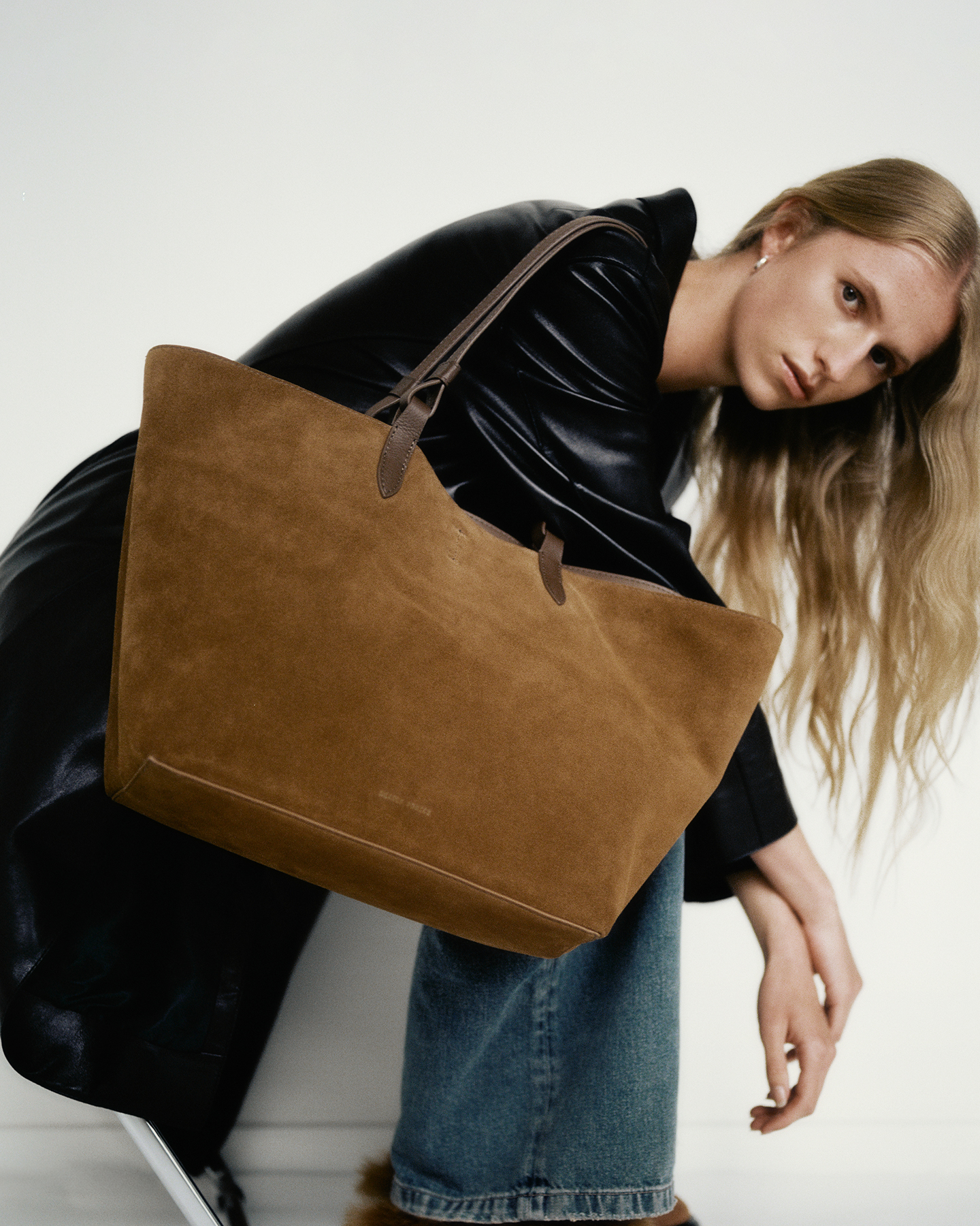 Person with long hair holding a large brown suede bag.