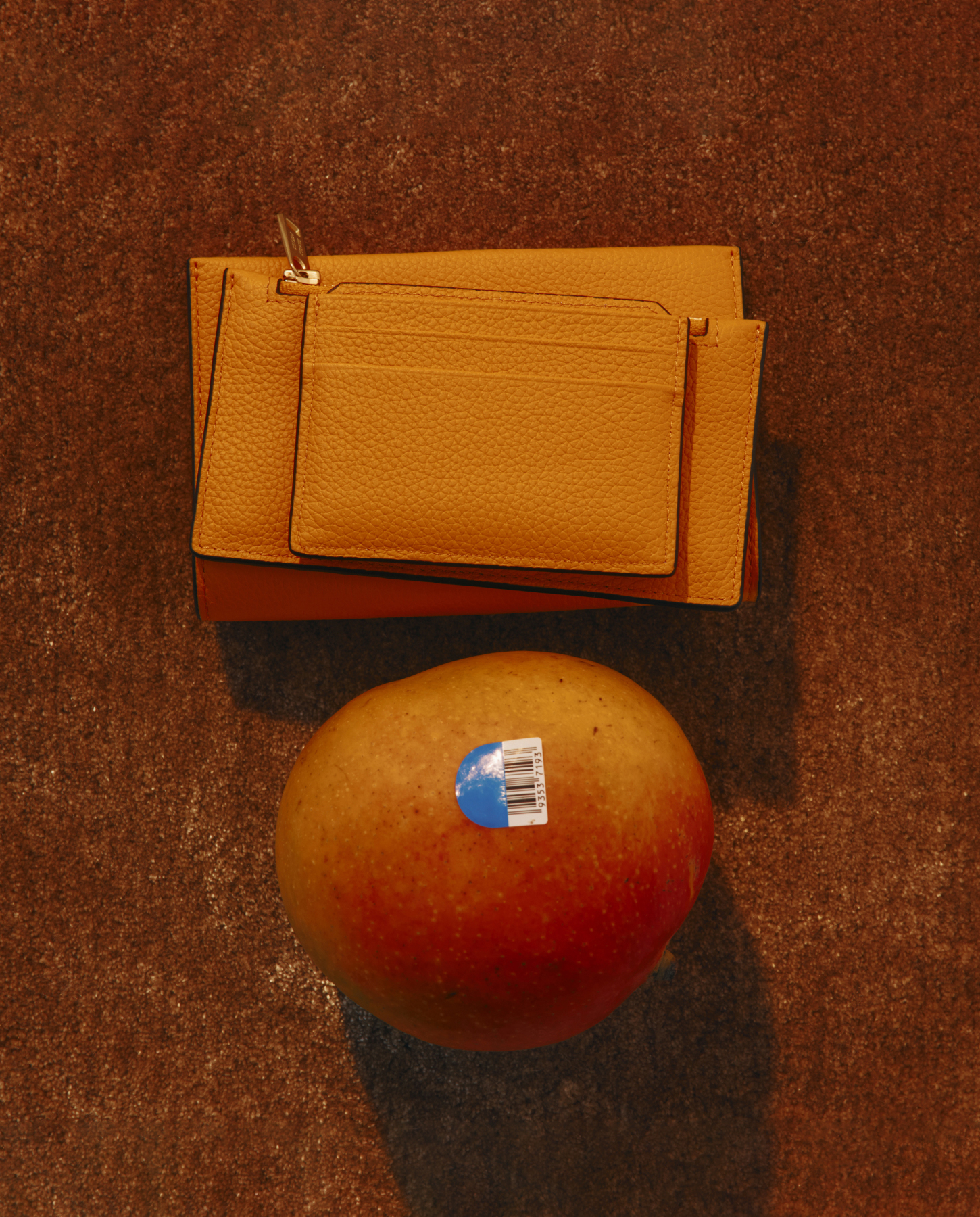 Yellow wallet and mango with sticker on a brown surface.