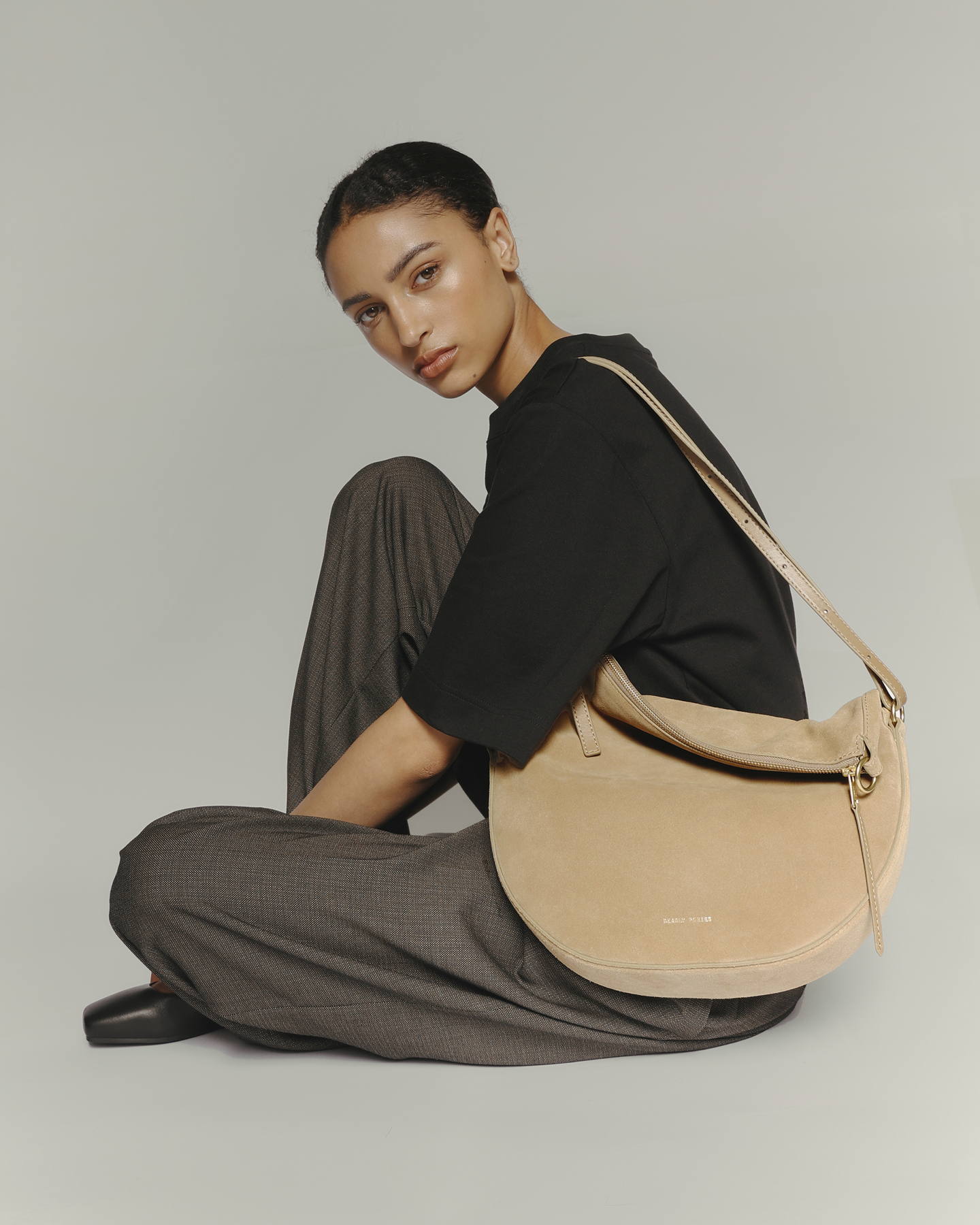 Person seated with a tan shoulder bag, wearing a black shirt and gray pants.