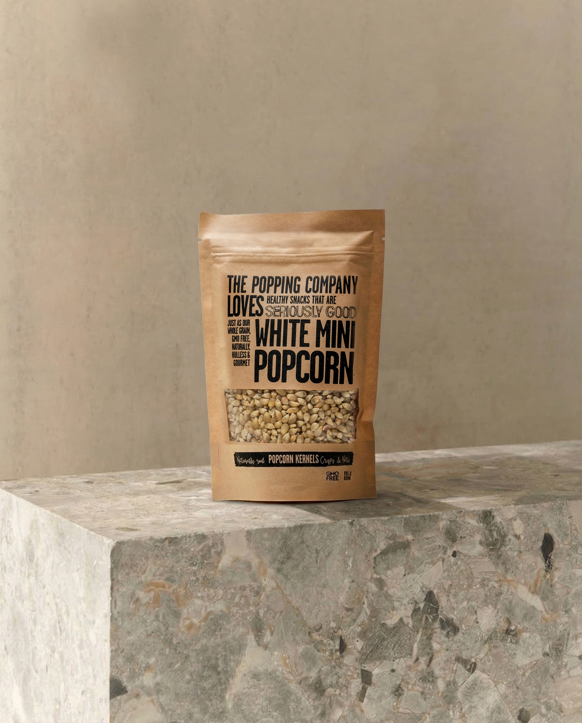 A brown paper bag of The Popping Company White Mini Popcorn sitting on a marble block.