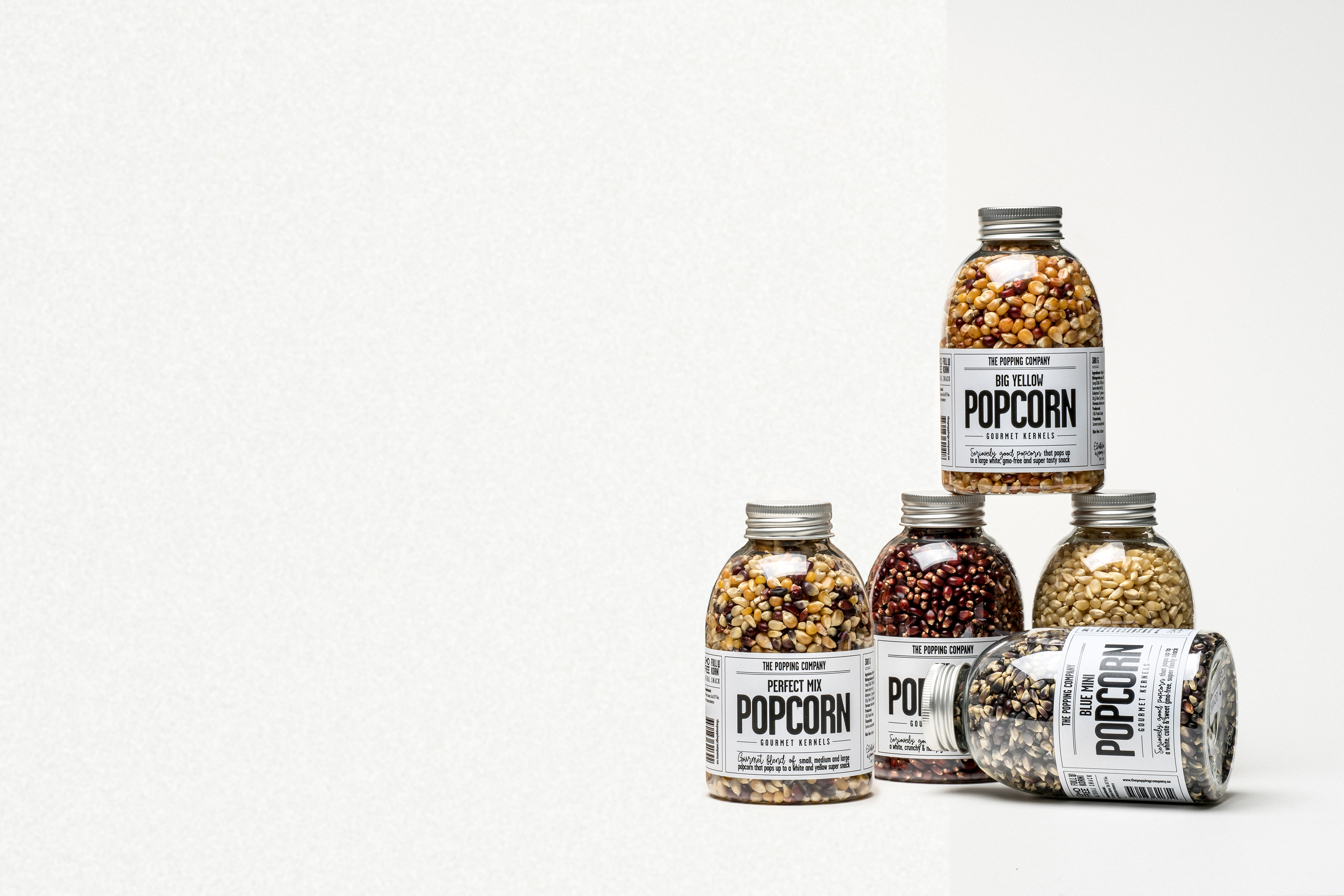 An assortment of gourmet popcorn kernels and seasonings in various bags, jars, and shakers on a white background.