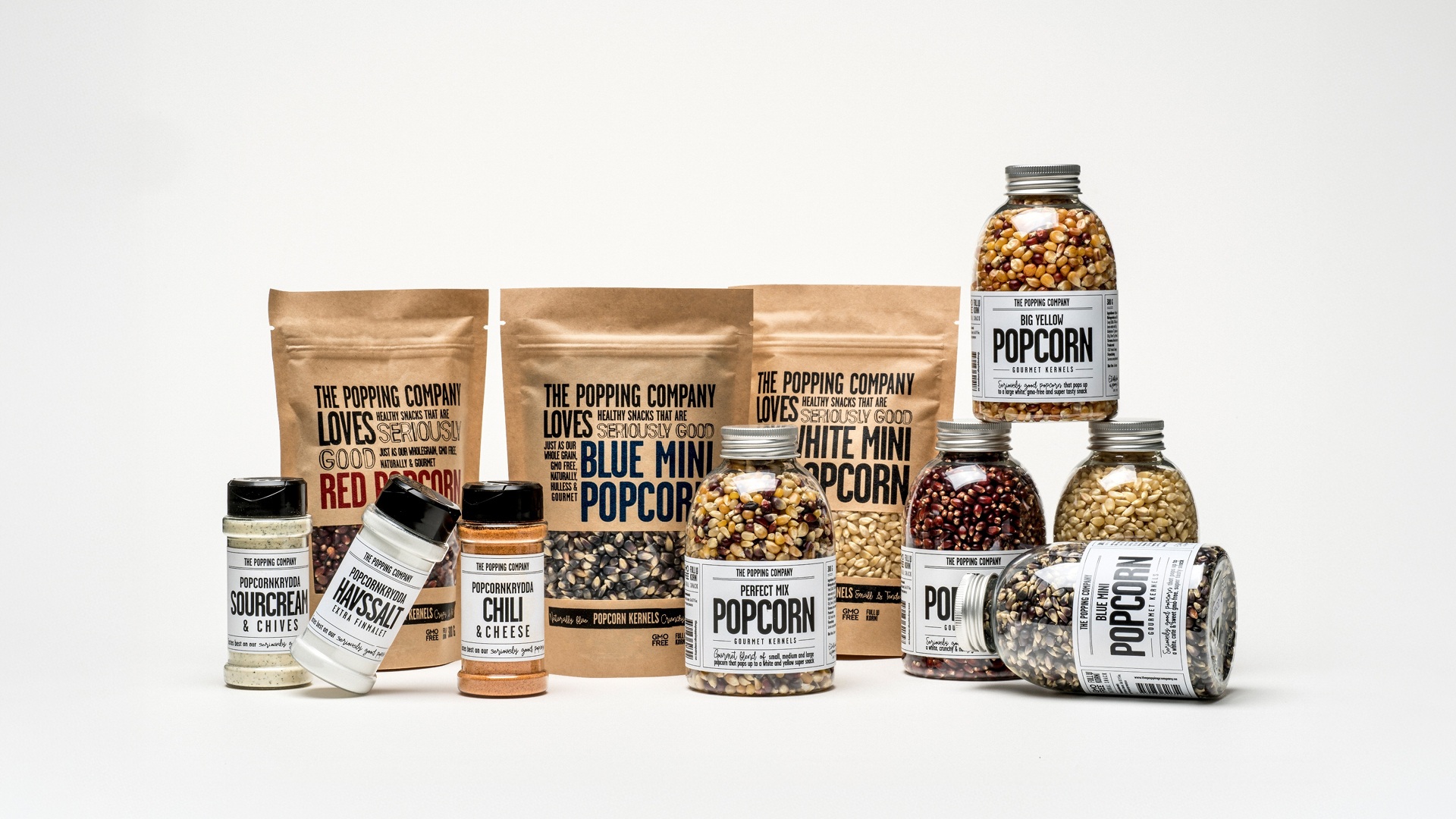An assortment of gourmet popcorn kernels and seasonings in various bags, jars, and shakers on a white background.