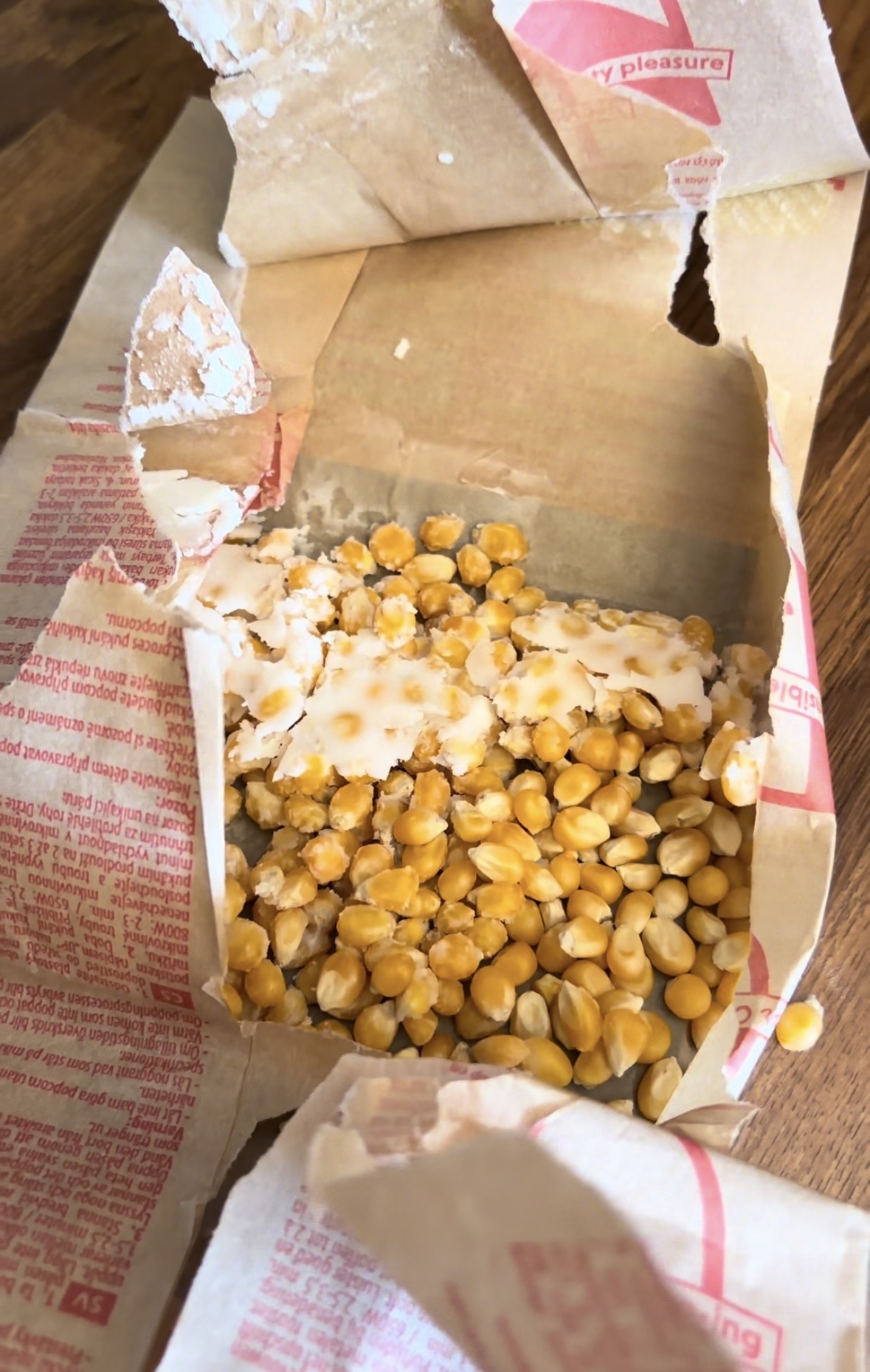 A torn-open paper bag of microwave popcorn filled with unpopped kernels.