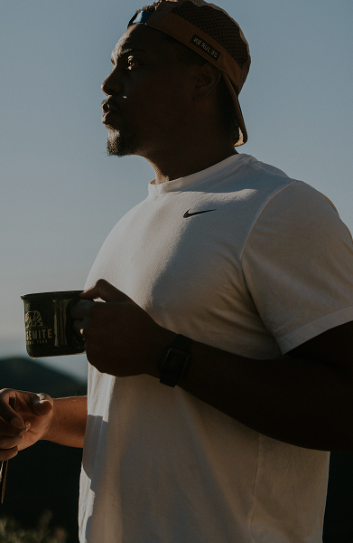 Person wearing a cap, holding a mug, silhouetted against the sky.