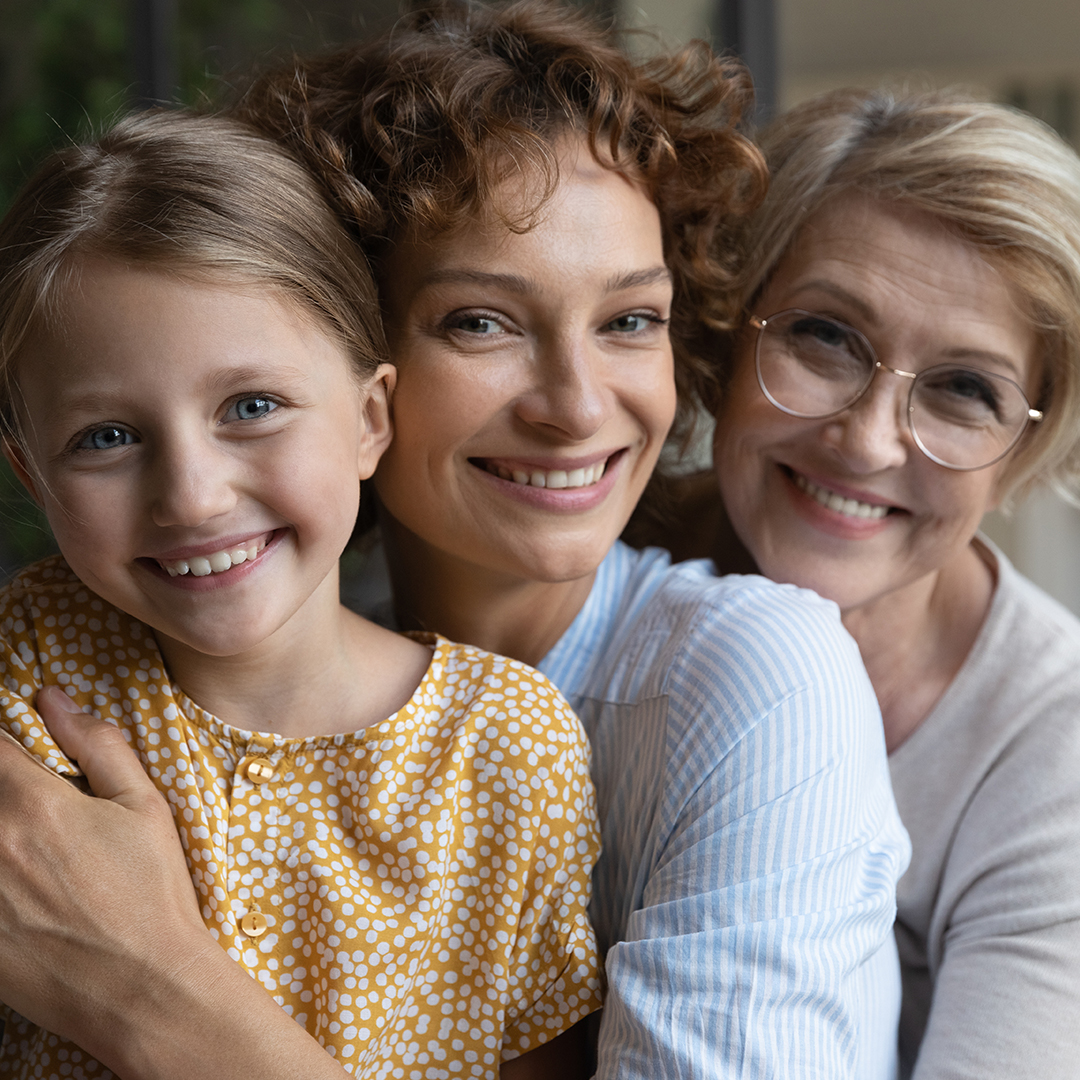 Three smiling people, two adults and a child, close together indoors.