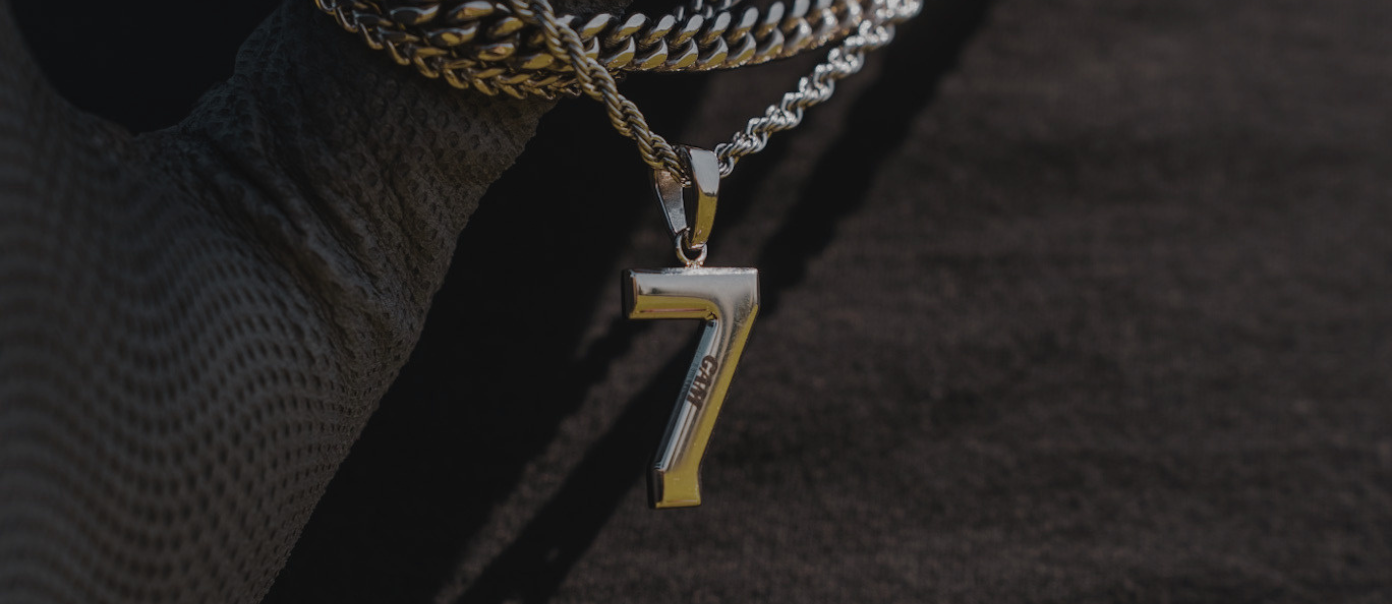 A close-up of a person wearing silver chains and a number seven pendant against a black shirt.