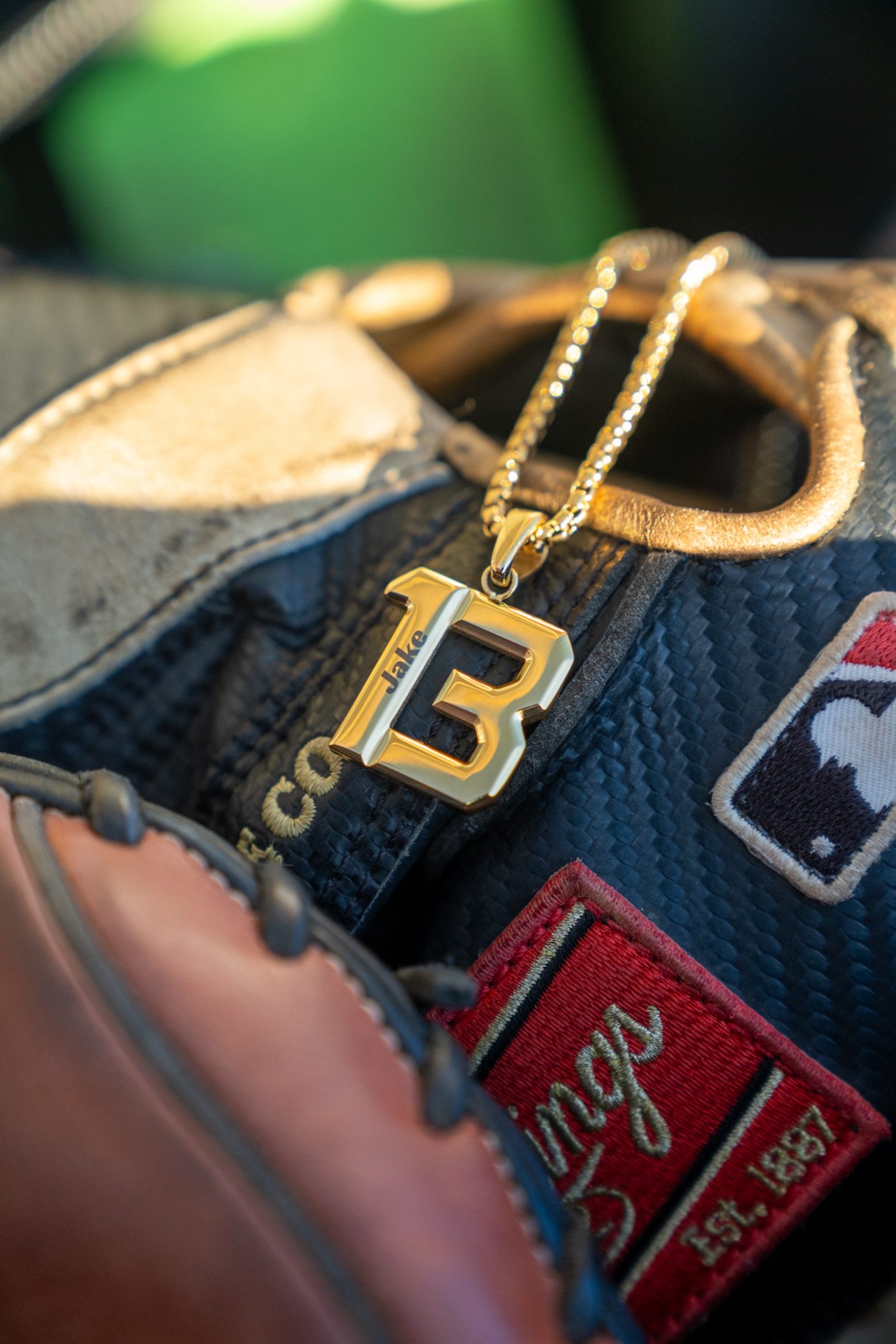 A gold necklace with a 'B' pendant engraved with 'Jake' rests inside a Rawlings baseball glove.