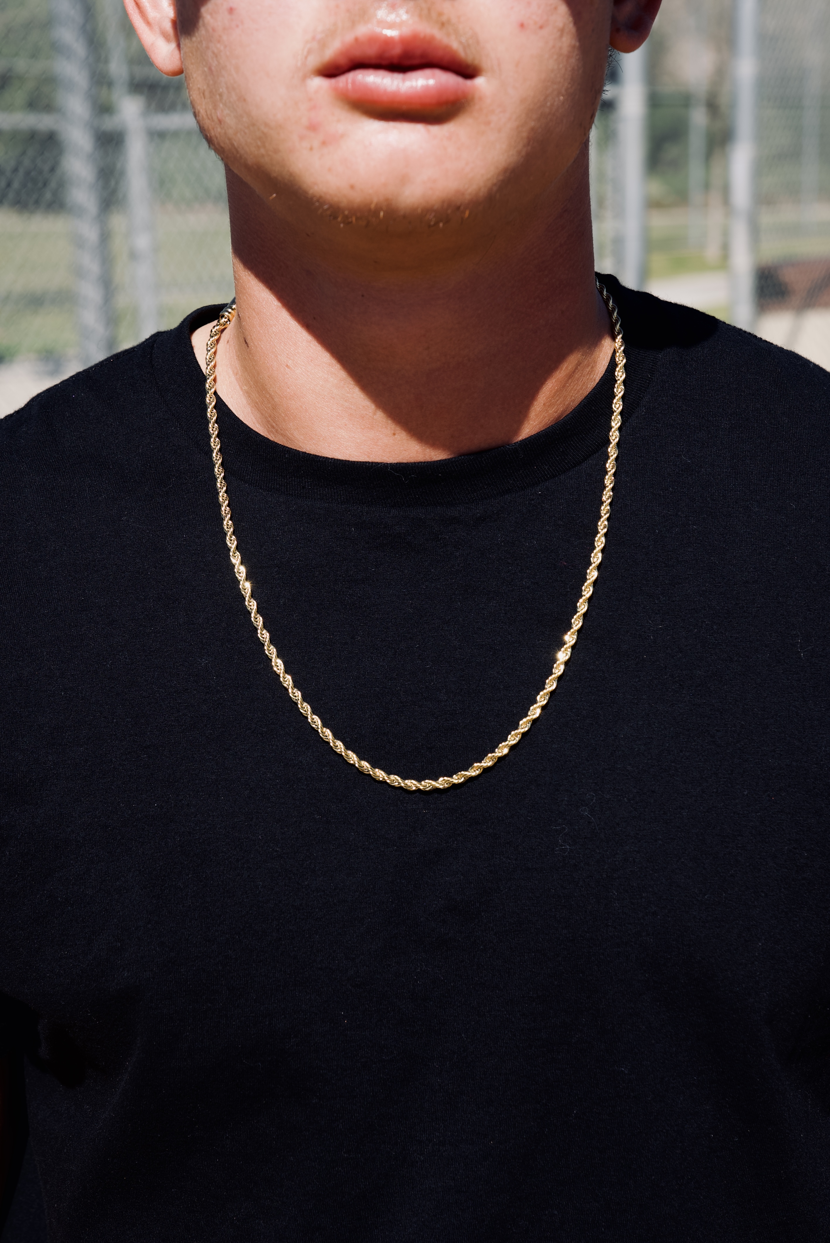 A close-up of a man wearing a black t-shirt and a gold rope chain necklace.
