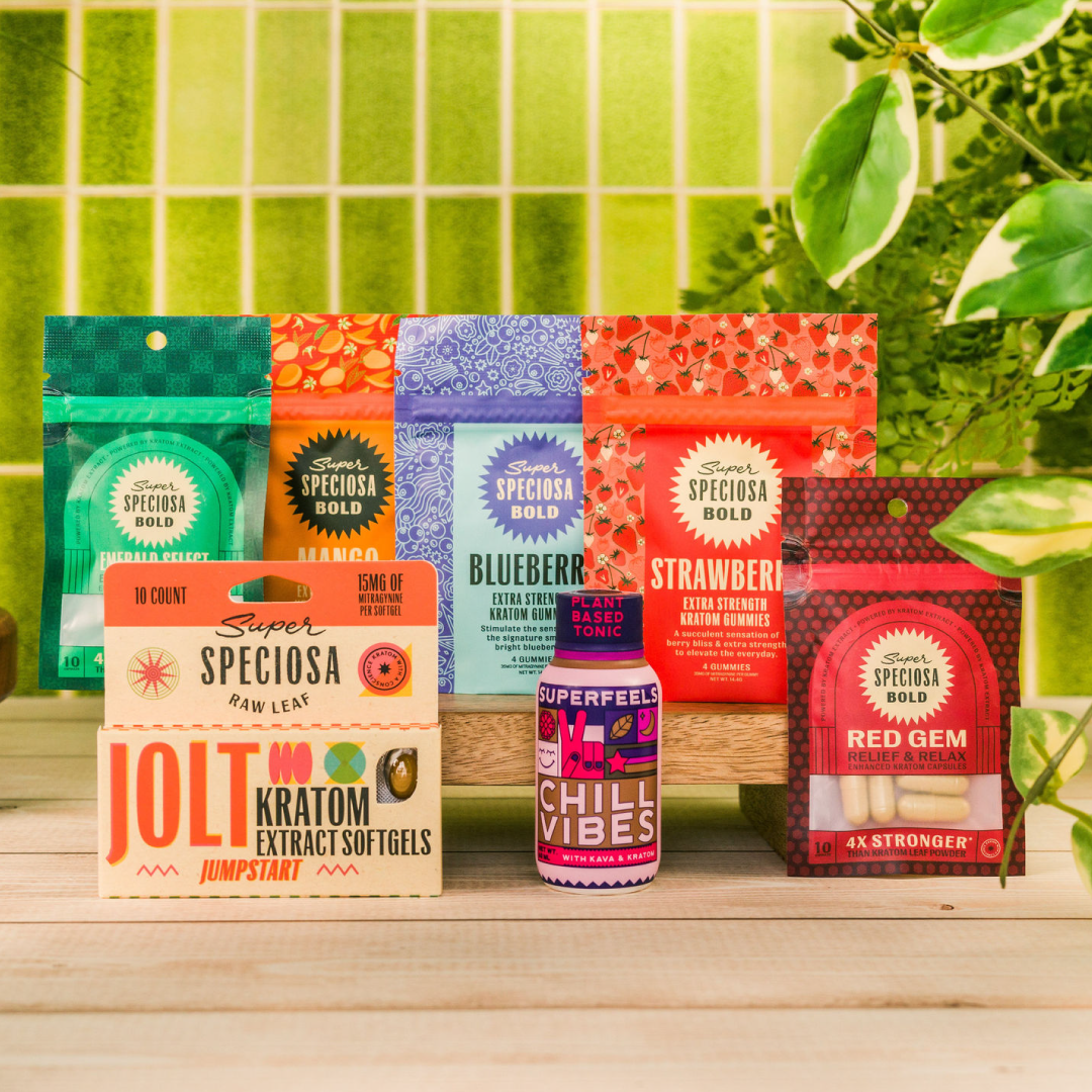 Assorted kratom product packages displayed on a wooden surface with green plants in the background.