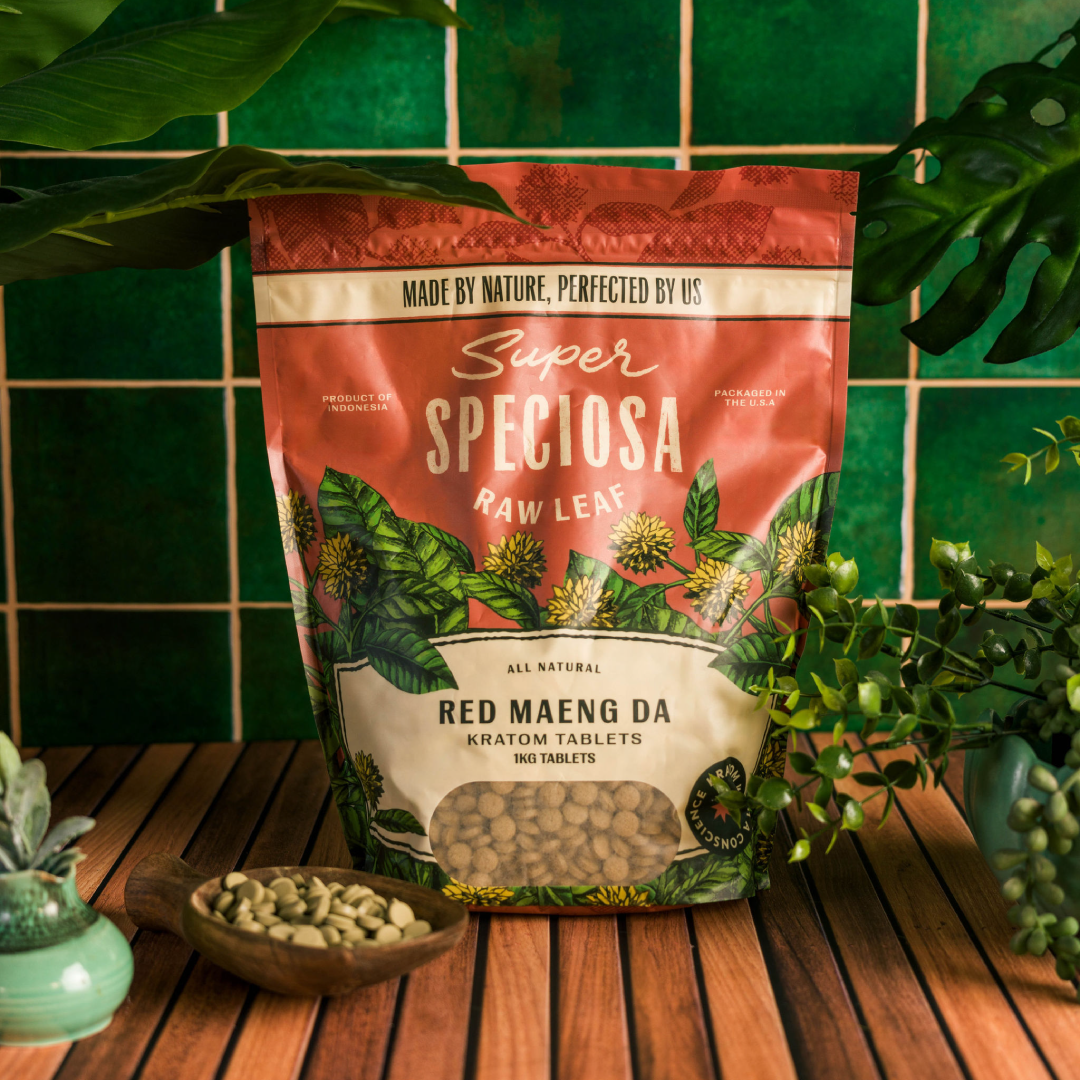 Bag of Super Speciosa Red Maeng Da kratom tablets on a wooden table with plants.