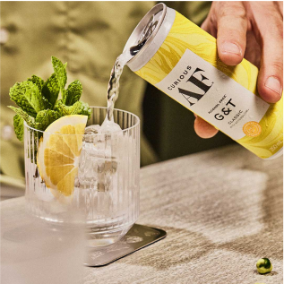 Pouring a canned gin and tonic into a glass with lemon and mint.