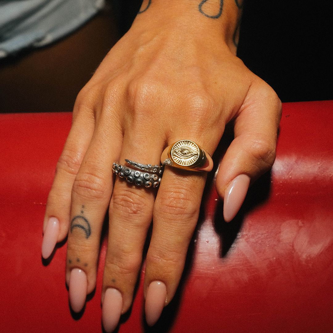 Hand with tattoos and two unique rings on a red surface.