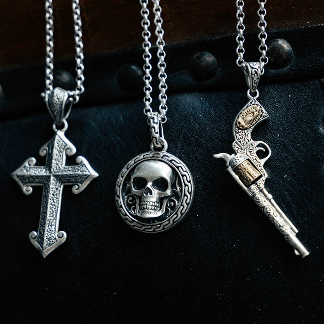 Three silver necklaces: a cross, a skull medallion, and a decorated gun pendant on chains.