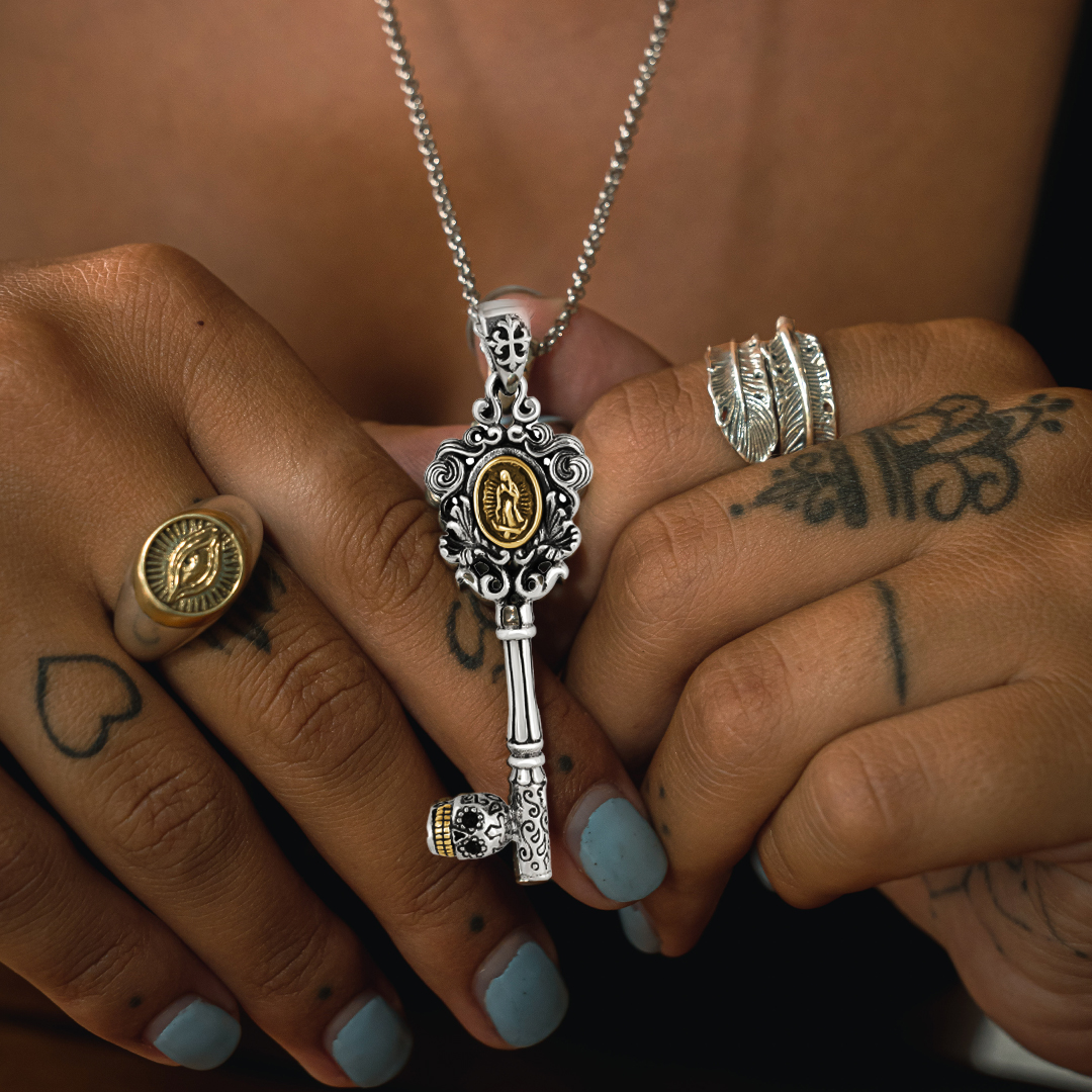 Ornate key necklace and rings on tattooed hands with blue nails.