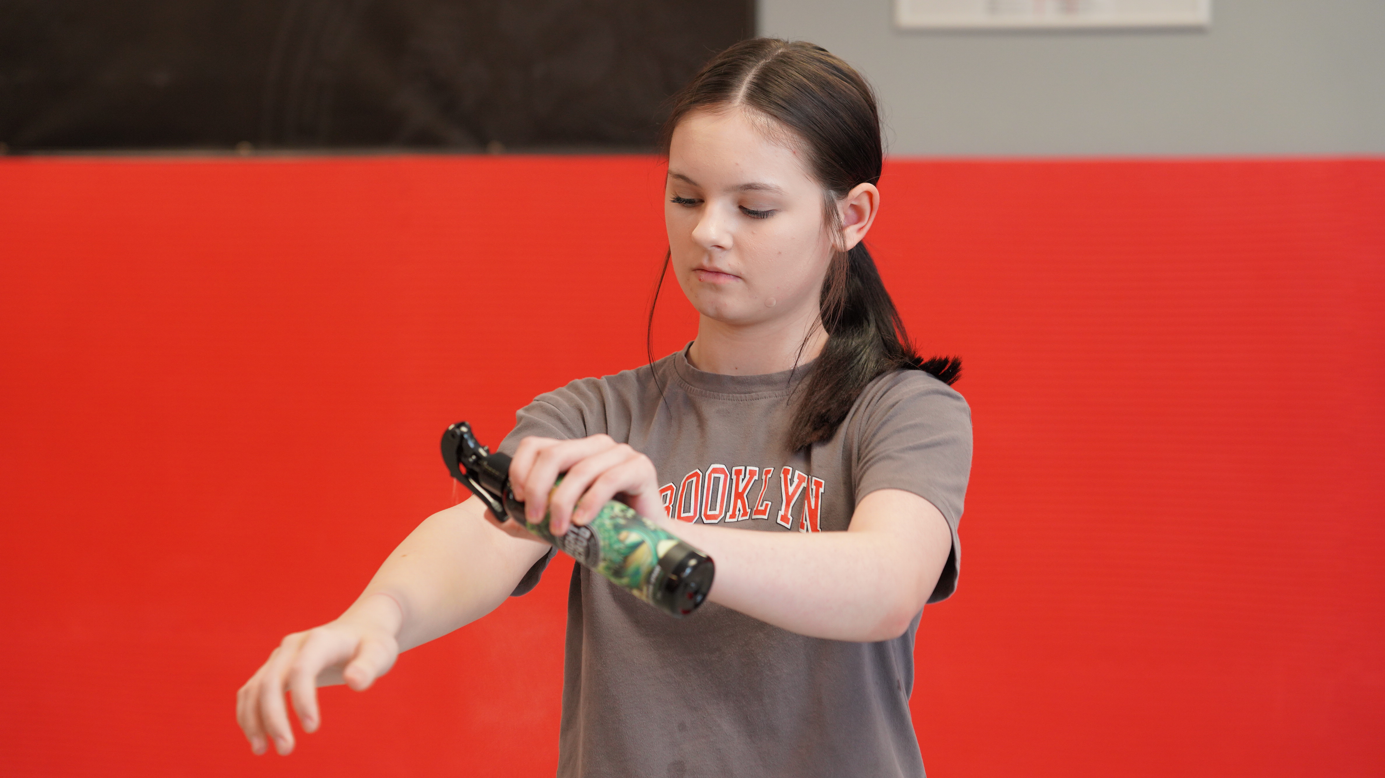 Person using a spray bottle on their arm in front of a red background.