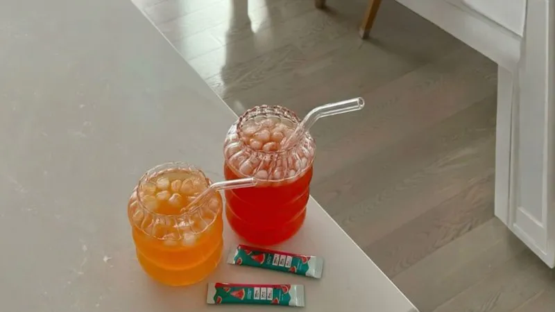 Two drinks with ice and straws on a table, beside two small packets.