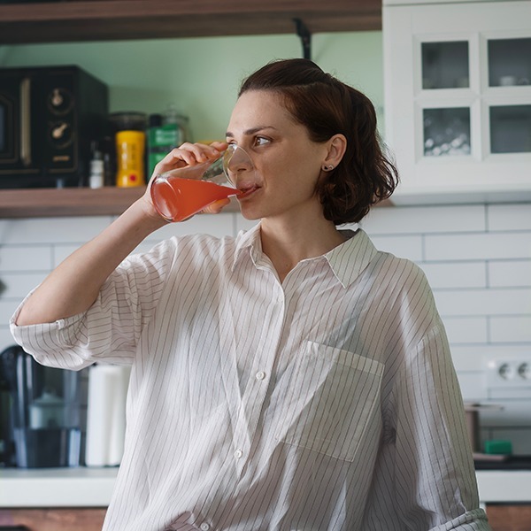 Person drinking red beverage in a kitchen.