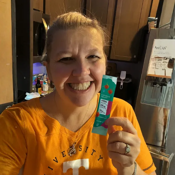 Smiling person holding a small product packet in a kitchen setting.
