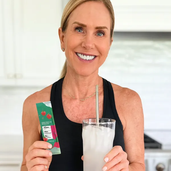 Woman holding a drink and a packet in a kitchen.