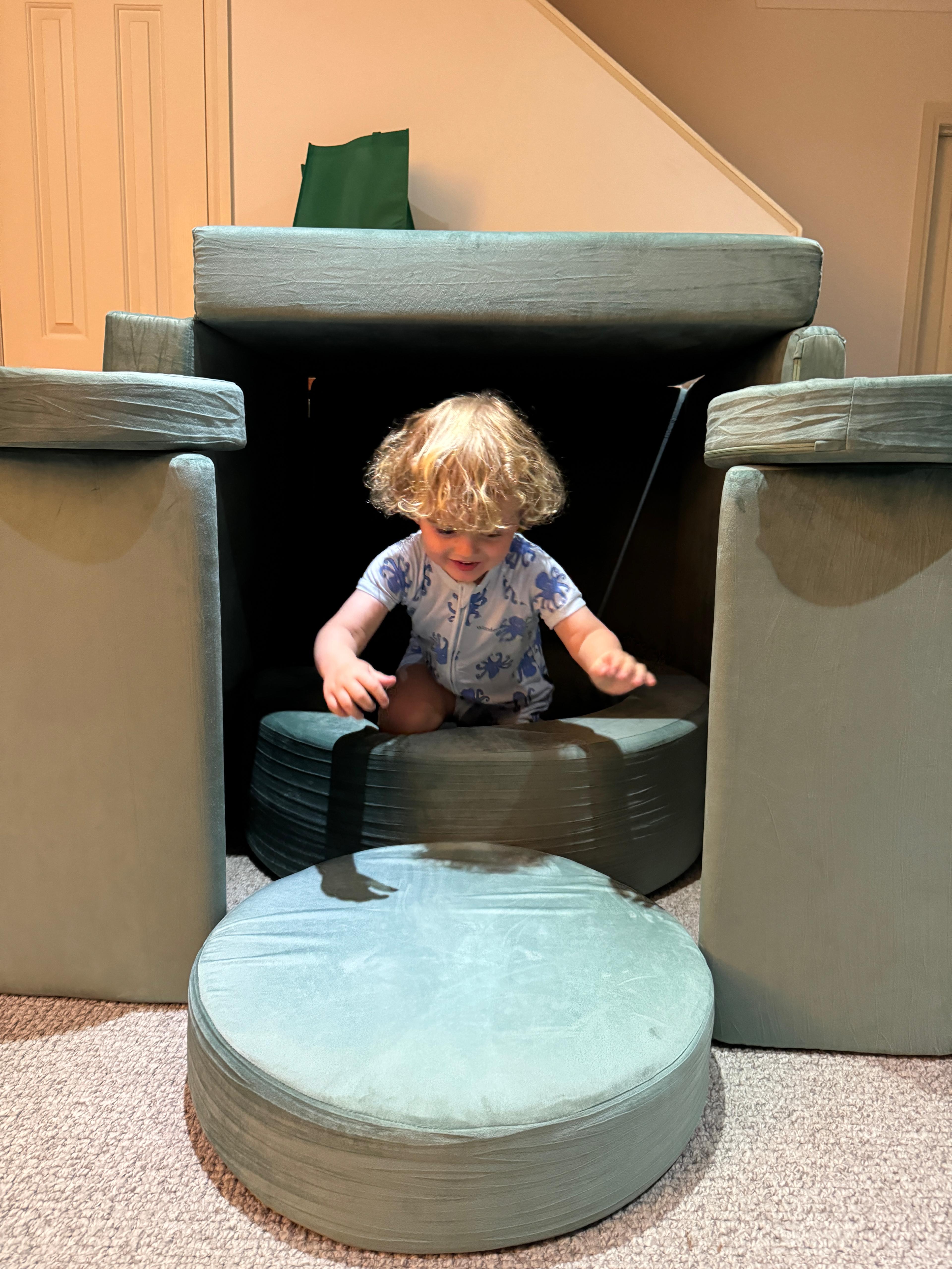 Child playing inside a fort made of green cushions.