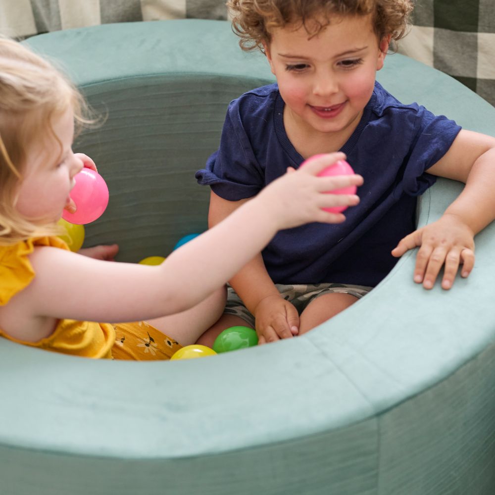 Two children playing with colorful balls in a soft play area.