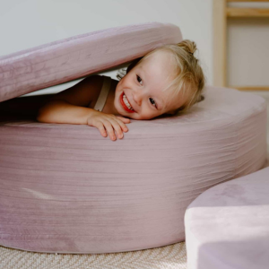 Child smiling while lying between soft, round cushions.