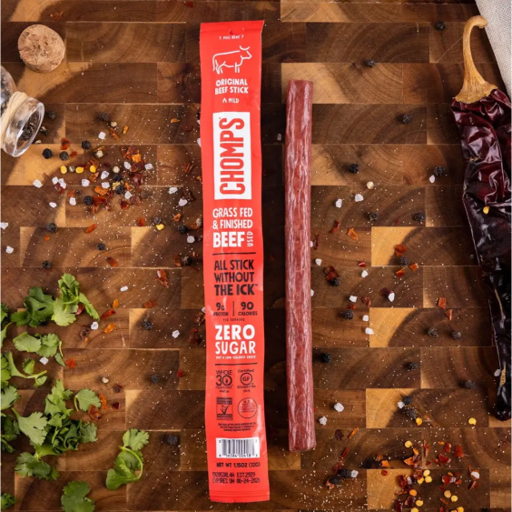 Beef stick and packaging on a wooden board with herbs and spices.
