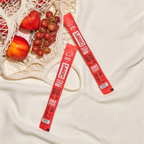 Chomps beef sticks with fruits in a reusable net bag on a textured surface.