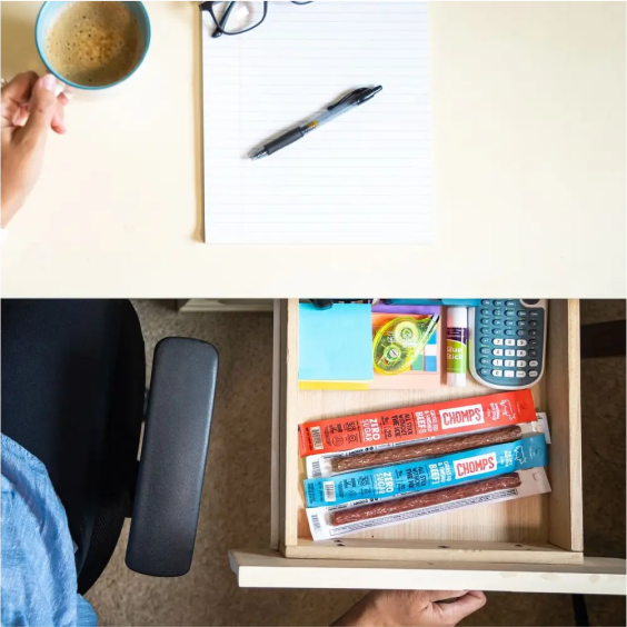 Desk with coffee, notebook, pen, and a drawer containing snacks and stationery items.