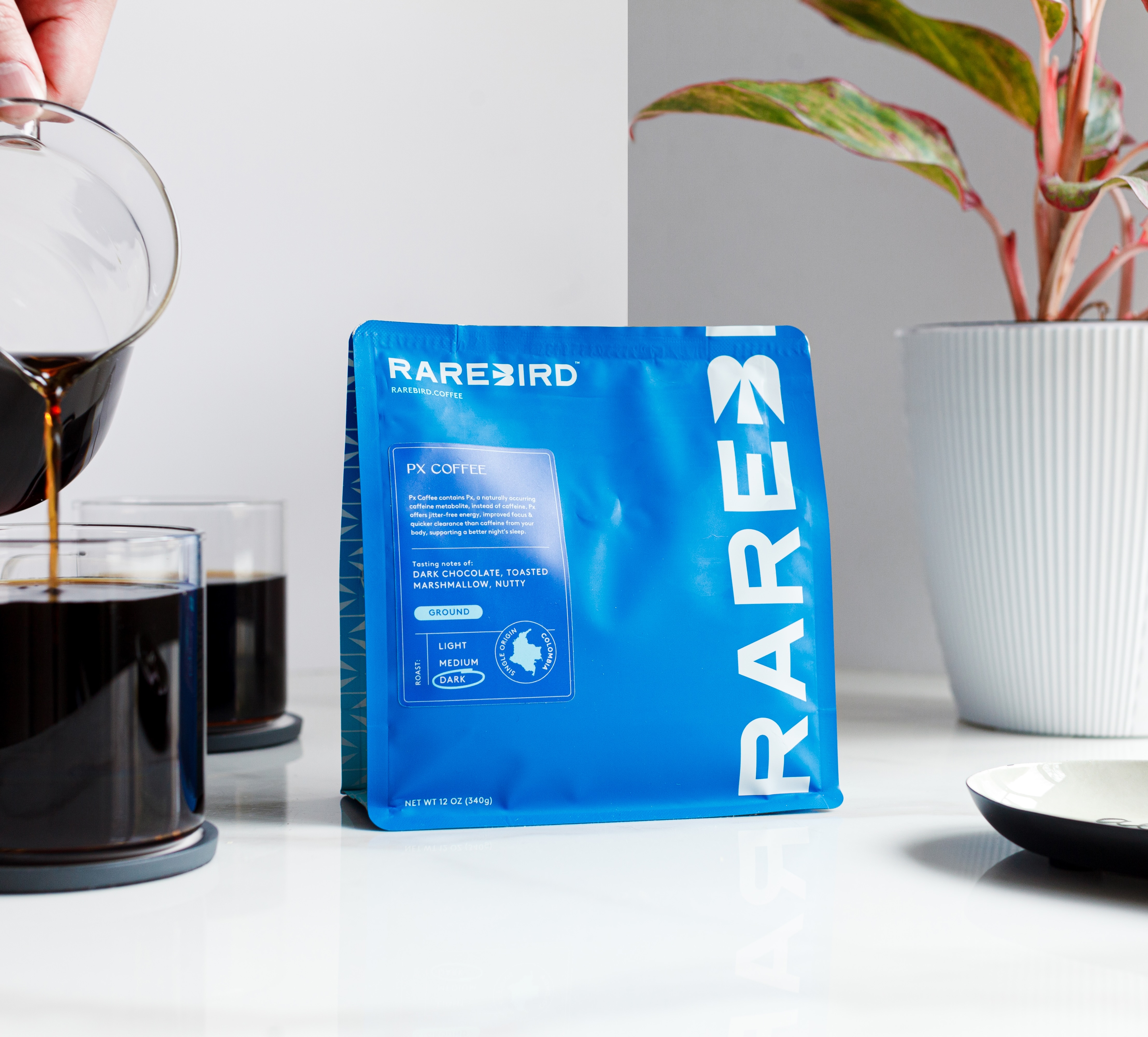 Blue coffee bag beside a glass of poured coffee on a white surface.