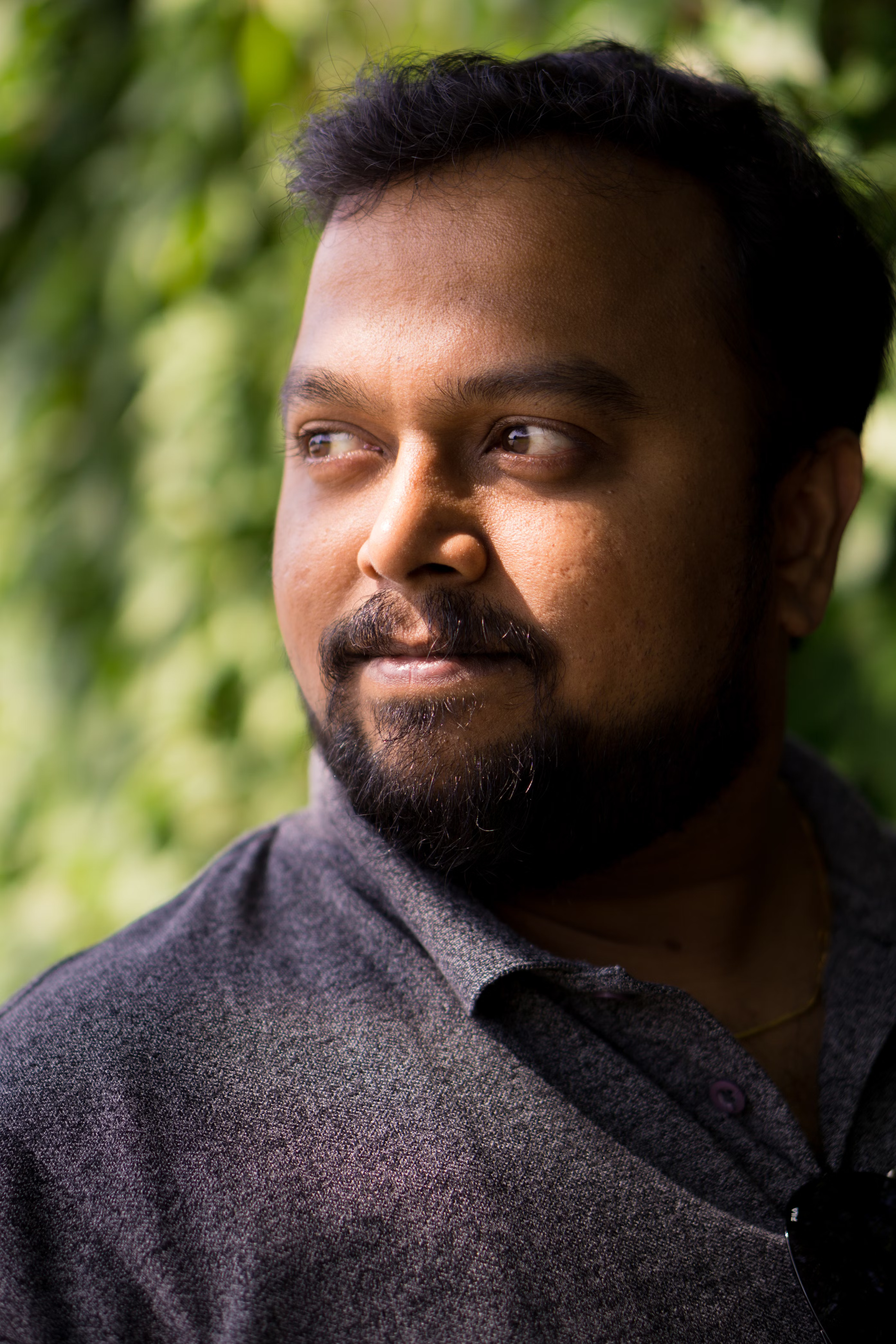 Man looking to the side, surrounded by greenery.