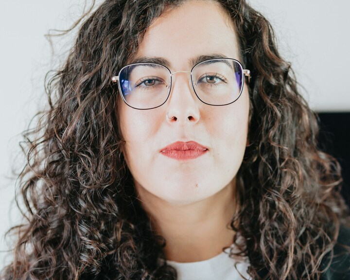 Person with curly hair and glasses looking at the camera.