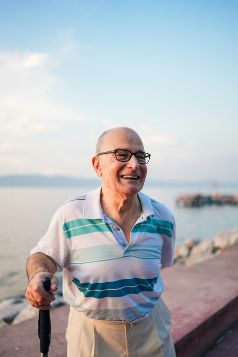 Smiling man with glasses and a cane by the waterfront.