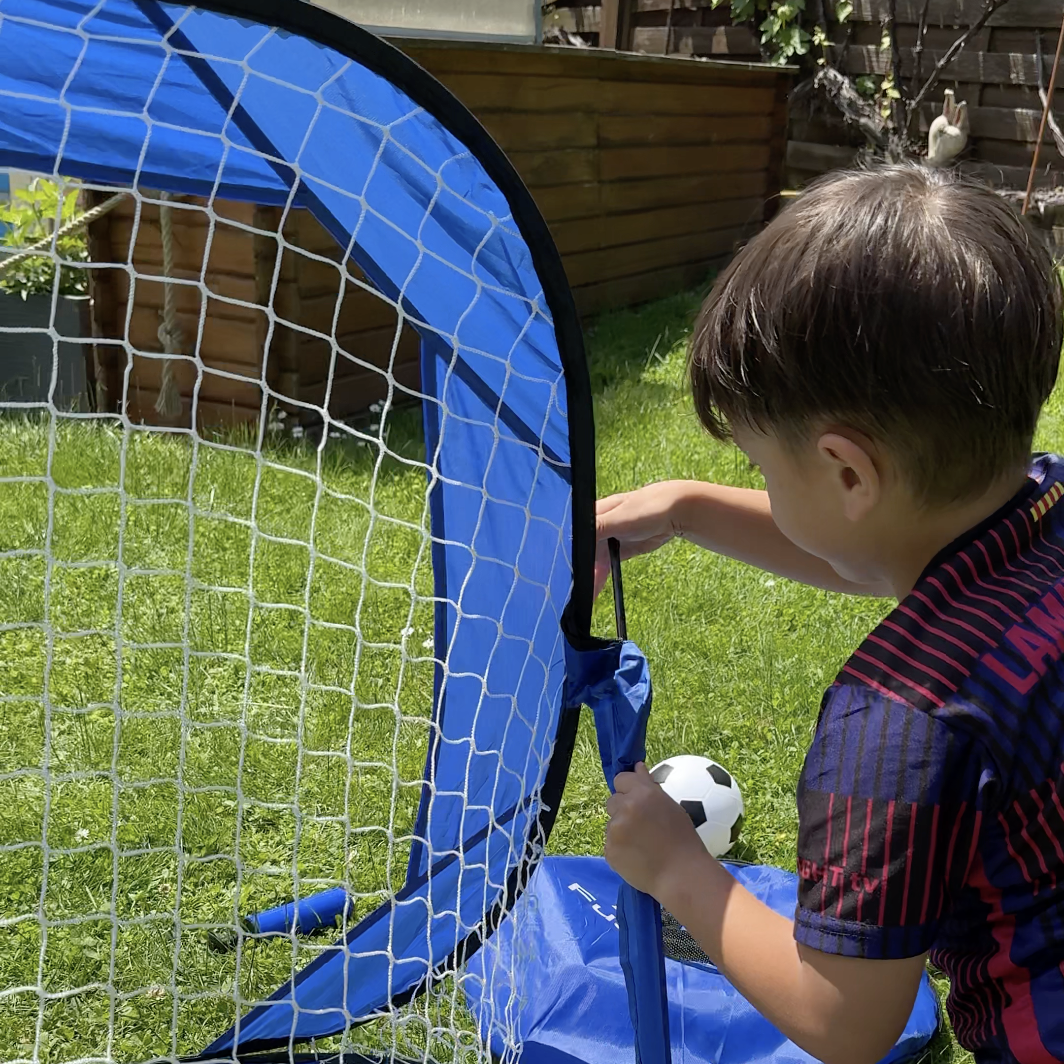 Child setting up a blue soccer goal in a garden.