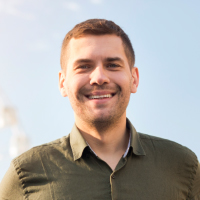 A headshot of a smiling young man with short brown hair, wearing a green collared shirt outdoors.