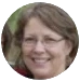 A circular, cropped headshot of a smiling woman with brown hair and glasses.