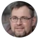 A circular headshot of a man with glasses and a goatee.