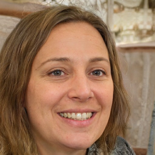 A close-up portrait of a smiling woman with light brown hair and light-colored eyes.