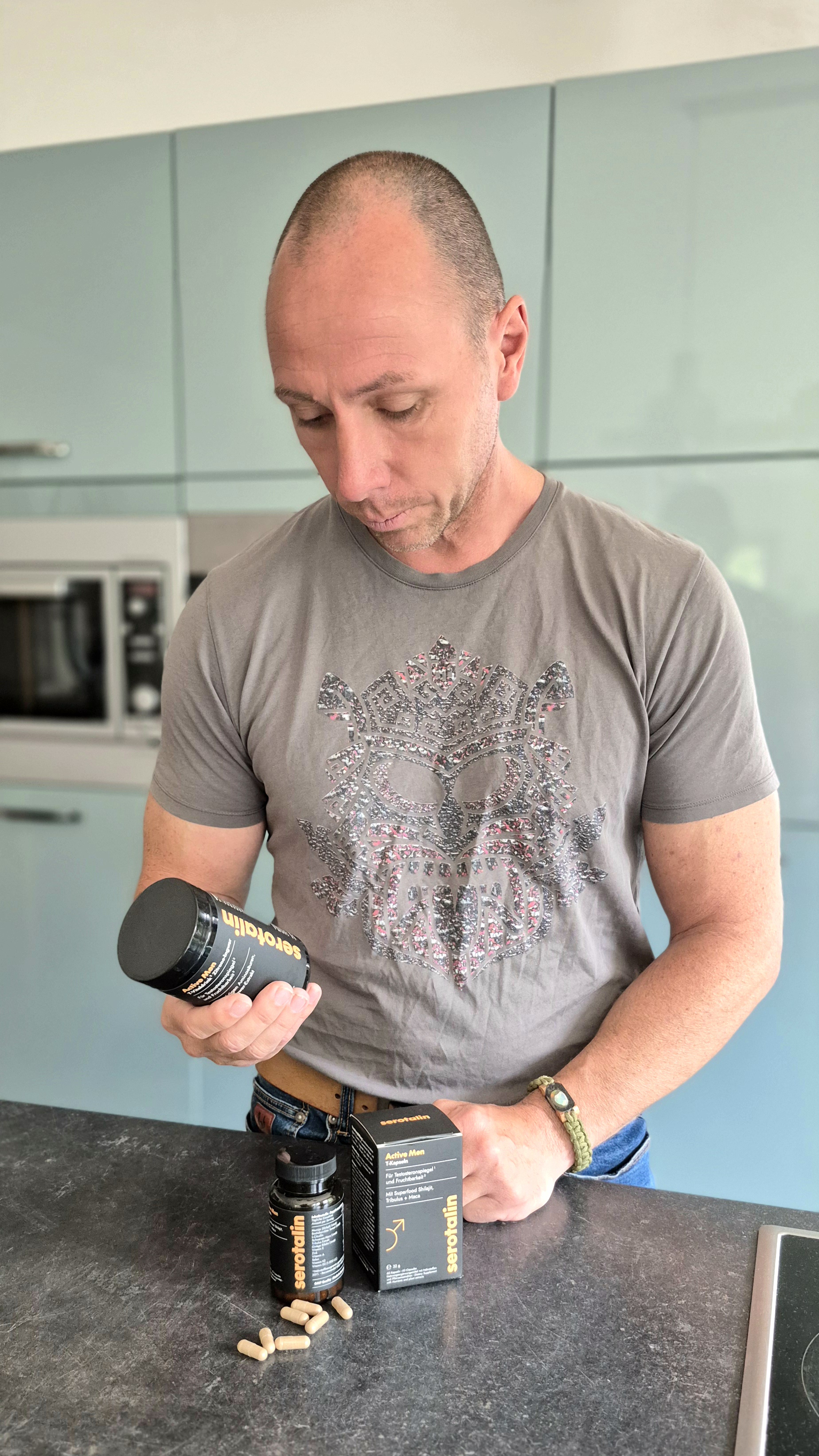 Man examining supplement bottle in kitchen with capsules on counter.