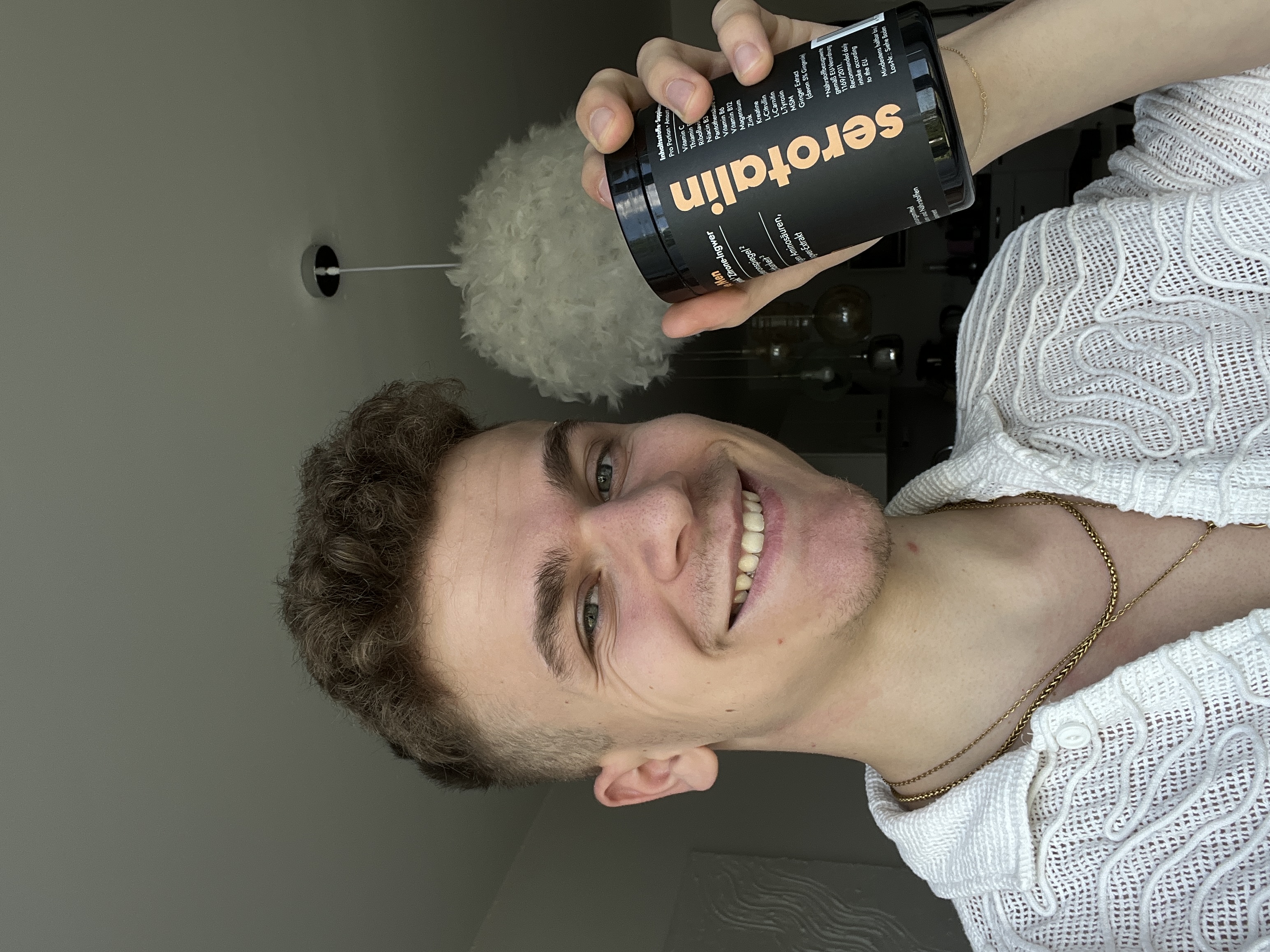 Person smiling and holding a container labeled 'serotalin' indoors.