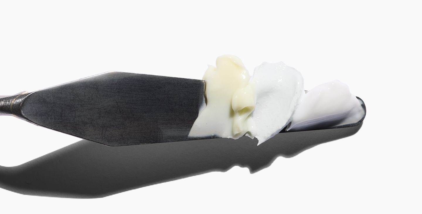 Metal spatula with white and cream substances on a plain background.
