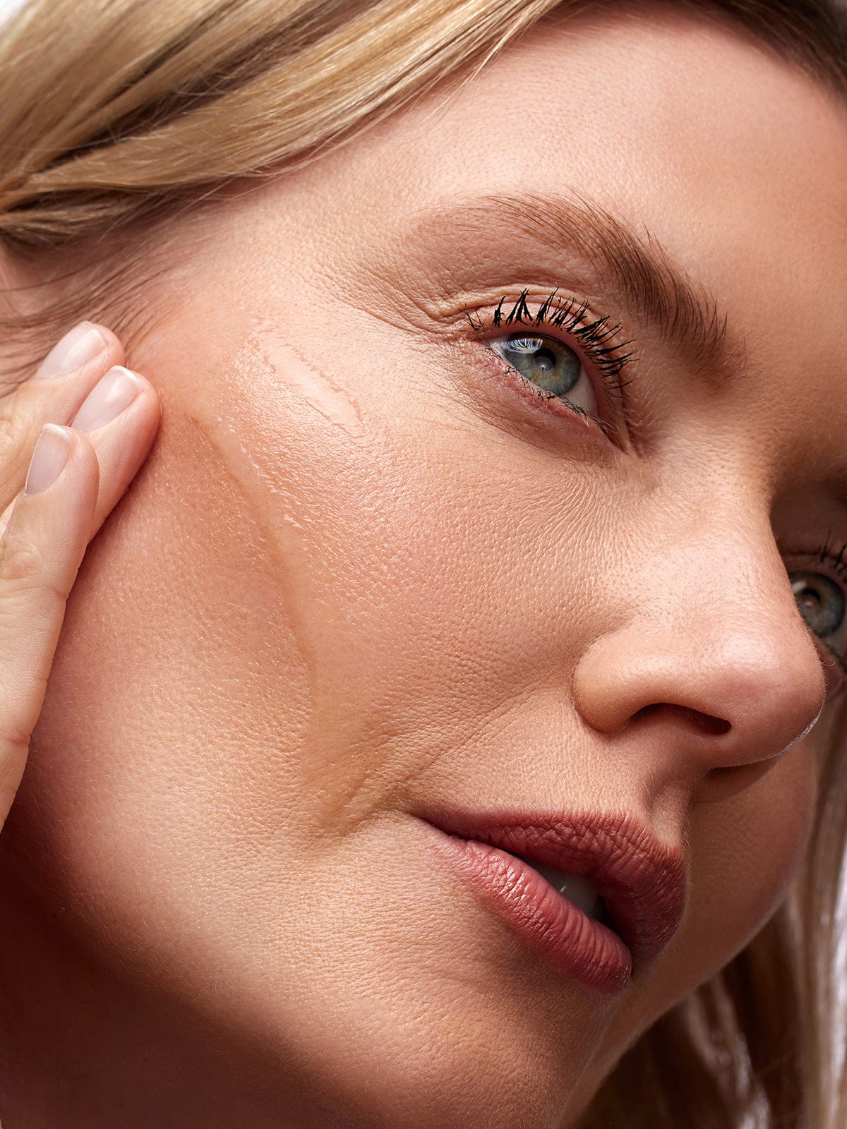 Close-up of a woman's face touching her cheek with visible skin texture.