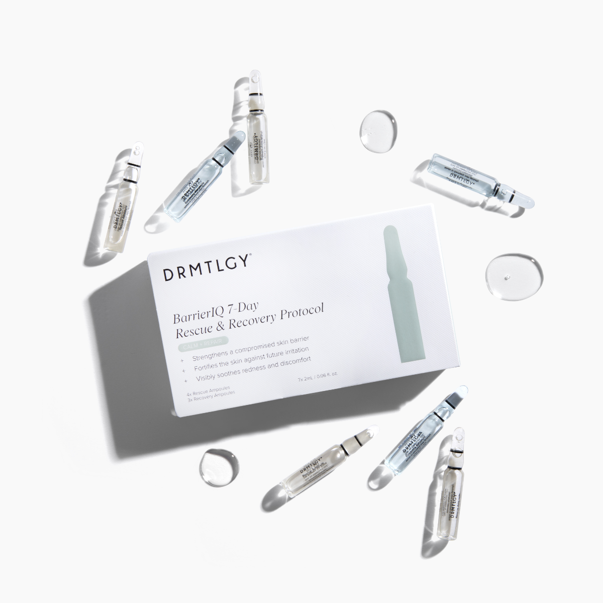 A flat lay of a DRMTLGY skincare box surrounded by seven glass ampoules and clear liquid droplets.
